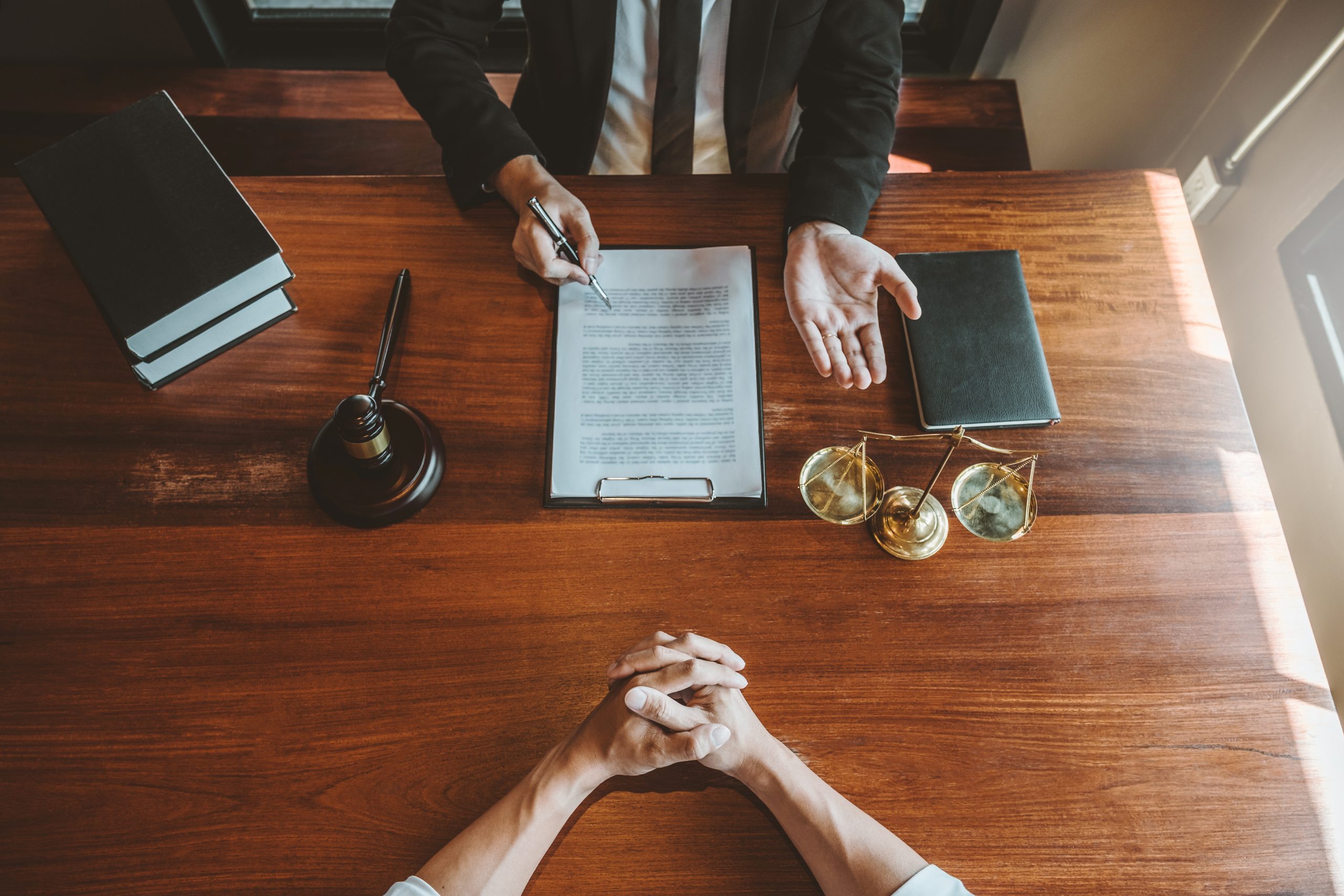 two people discussing some paperwork, with a gavel and a stack of books on the side of the person with a clipboard and a pen marking up the paperwork