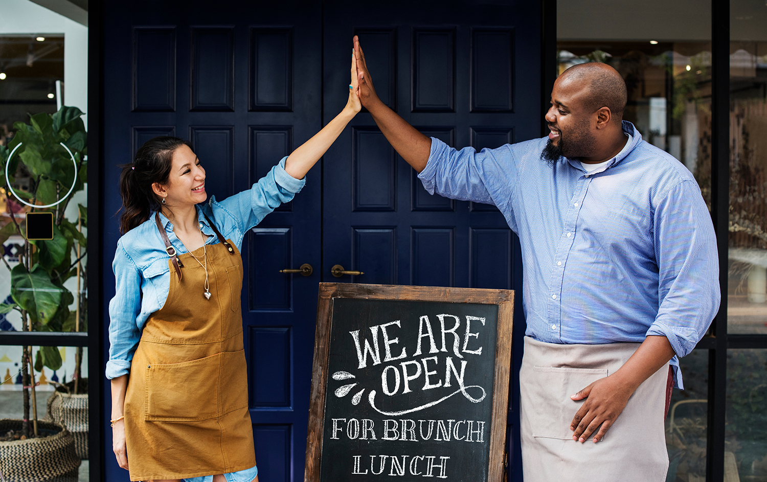 Two people high five over their “we are open for brunch and lunch” sign.