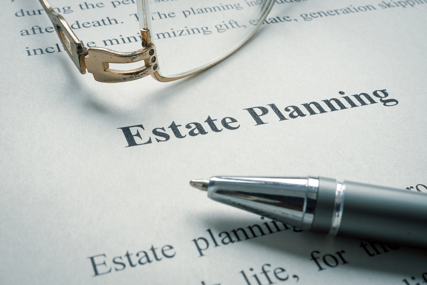 An image of a paper that says “Estate Planning” on it, with glasses and a pen.